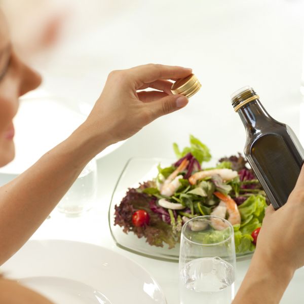 Woman holding oil above salad on table