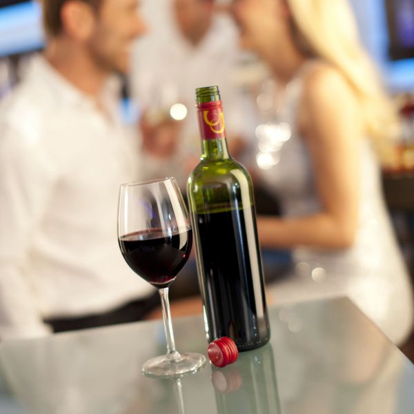Red wine glass and bottle with people in background